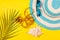 Top view on striped hat, sunglasses and measuring tape with a seashell and a palm branch on a bright yellow background