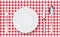 Top view of table place setting for dinner on red tablecloth with empty plate glasses and cutlery.