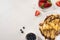 Top view of tasty crepes with chocolate spread and walnuts on plate near bowls with blueberries and strawberries