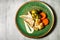 top view on tasty hake fillet with vegetables and sauce served on green plate