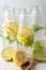 Top view of three bottles with water, lemon slices, lime and mint, on white table with half lemons and wooden spoon with brown sug