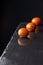 Top view of three wet small kumato tomatoes, with selective focus, on black slate with reflection, black background, vertical