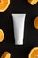 Top view of a tube of cream surrounded by oranges on a black background