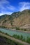 Top view of the turquoise river flowing through a hilly valley and a dirt road running along the coast