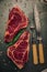 Top view of two bloody pieces of steak with rosemary and cutlery