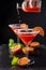 Top view of two cocktail glasses with unfocused bottle serving drops of blood orange martini, half orange and mint, on black backg