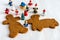 Top view of two gingerbread cookies with figurines, the first ones focused, the others in bokeh, on white baking paper background
