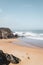 Top view of two people standing at the beach while the foamy shallow sea waves approach the coast