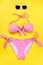 Top view of two pieces pink chequered swimming suit and white sunglasses over yellow background.