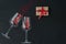 Top view of two wine glasses with little red heart sparkling confetti and wrapped giftbox on black background, lots of copy space