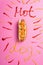 Top view of unhealthy hot dog on pink with word hot dog written with ketchup and mustard.