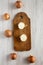 Top view, unpeeled raw yellow onions on rustic wooden board over white wooden surface, top view. Flat lay, overhead, from above