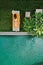 Top view of unrecognizable slim young woman in beige bikini relaxing and sunbathe near luxury swimming pool in green tropic in