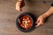 Top view of unrecognizable woman holding and melting savory tomato soup with sour cream and croutons in black bowl.