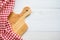 Top view of unused brand new brown handmade wooden cutting board and red napkins on white wooden table background - Food and kitch