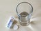 Top view of Upsarin C antipyretic tablets and glass of water on a white table. Soluble effervescent aspirin with vitamin C pills