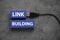 Top view of a usb cable and blue wooden cube written with Link Building on grey background