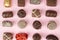 Top view of various chocolate pralines on pink background. Collection chocolates candy. Assorted chocolates on pink