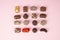 Top view of various chocolate pralines on pink background. Collection chocolates candy. Assorted chocolates on pink