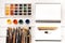 Top view of various paintbrushes, paints and blank open notebook