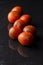 Top view of wet small kumato tomatoes, on black slate with reflection, black background, vertical,