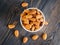 Top view of white bowl with a handful of almond, nuts on a wooden dark background.