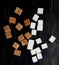 top view of white and brown sugar cubes scattered on dark wooden background
