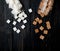 top view of white and brown sugar cubes scattered from glass jars on dark wooden background