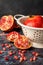 Top view of white colander with wet pomegranate on blue marble with pieces and pomegranate seeds, dark background