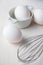 Top view of white eggs and metal whisk, with selective focus, on white wooden table