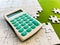 Top view, white puzzle and calculator on green background
