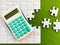 Top view, white puzzle and calculator on green background