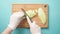 Top view of woman hand in glove cutting mango with zigzag knife on wooden cut board. Pastel blue background.
