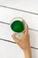 Top view of woman hand holding cup of chlorophyll drink on white wooden background. Vertical image