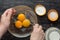 Top view of woman hands holding whisk and bowl with three yolks, starch, sugar and milk for mixing and making custard cream on the