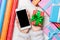 Top view of a woman holding a phone in one hand and a gift in another on wooden background. Rolled up wrapping paper and holiday