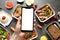 Top view of woman holding smartphone over grey table with lunchboxes, mockup for design. Healthy food delivery