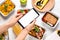 Top view of woman holding smartphone over white wooden table with lunchboxes. Healthy food delivery