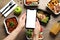 Top view of woman holding smartphone over wooden table with lunchboxes. Healthy food delivery