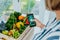 Top view woman holding wooden box with fresh vegetables and phone with active online mobile application with Veganuary
