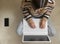 Top view of a woman working from home on the floor, typing at her laptop with a cellphone next to her. Telecommuting lifestyle