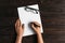 Top view of women`s hands, ready to write something on an empty piece of paper lying on a wooden table. Write a letter on a white