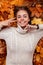 Top view of a wonderful young woman with a charming smile in a trendy knitted sweater on the background of orange-yellow foliage