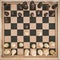 Top view on wooden chess board with chess figures ready for the game and man's hand making chess move on white wooden table