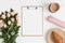 Top view of a wooden clipboard mockup with a bouquet of pink roses, coffee and a croissant on a white table