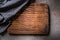 Top view of wooden dark brown vintage chopping board on dark metallic background with black checked cloth partial