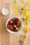 Top view of a wooden table with flower decoration, bowl of delicious red and fresh strawberries and a small bowl of fresh cheese