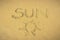 Top view of the word Sun written in the sand with a drawing representing it. Summer and weather concept