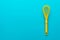 Top view of yellow plastic whisk over turquoise blue background with copy space