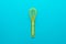 Top view of yellow plastic whisk over turquoise blue background with copy space